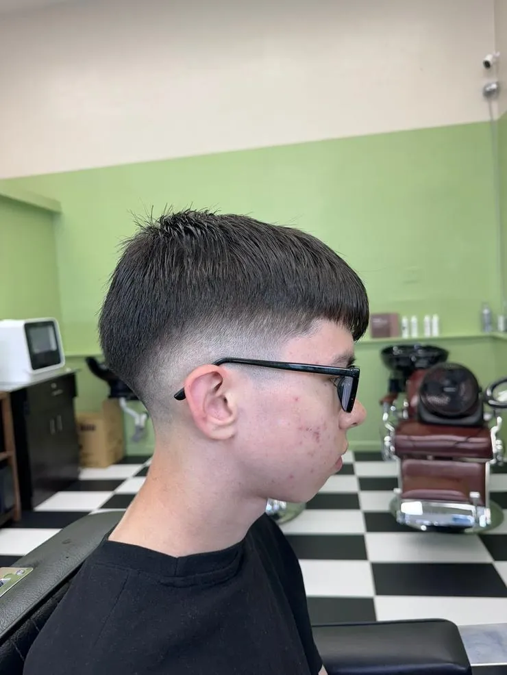 Side view of a teen with a mid taper fade and short fringe in the barber chair